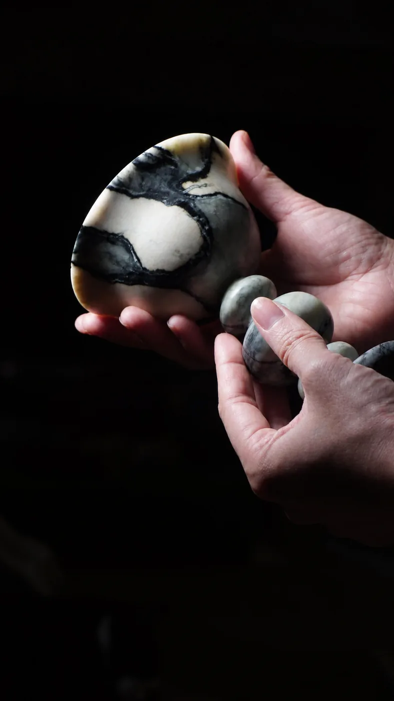 Hand-held sculptural marble objects against a dark background